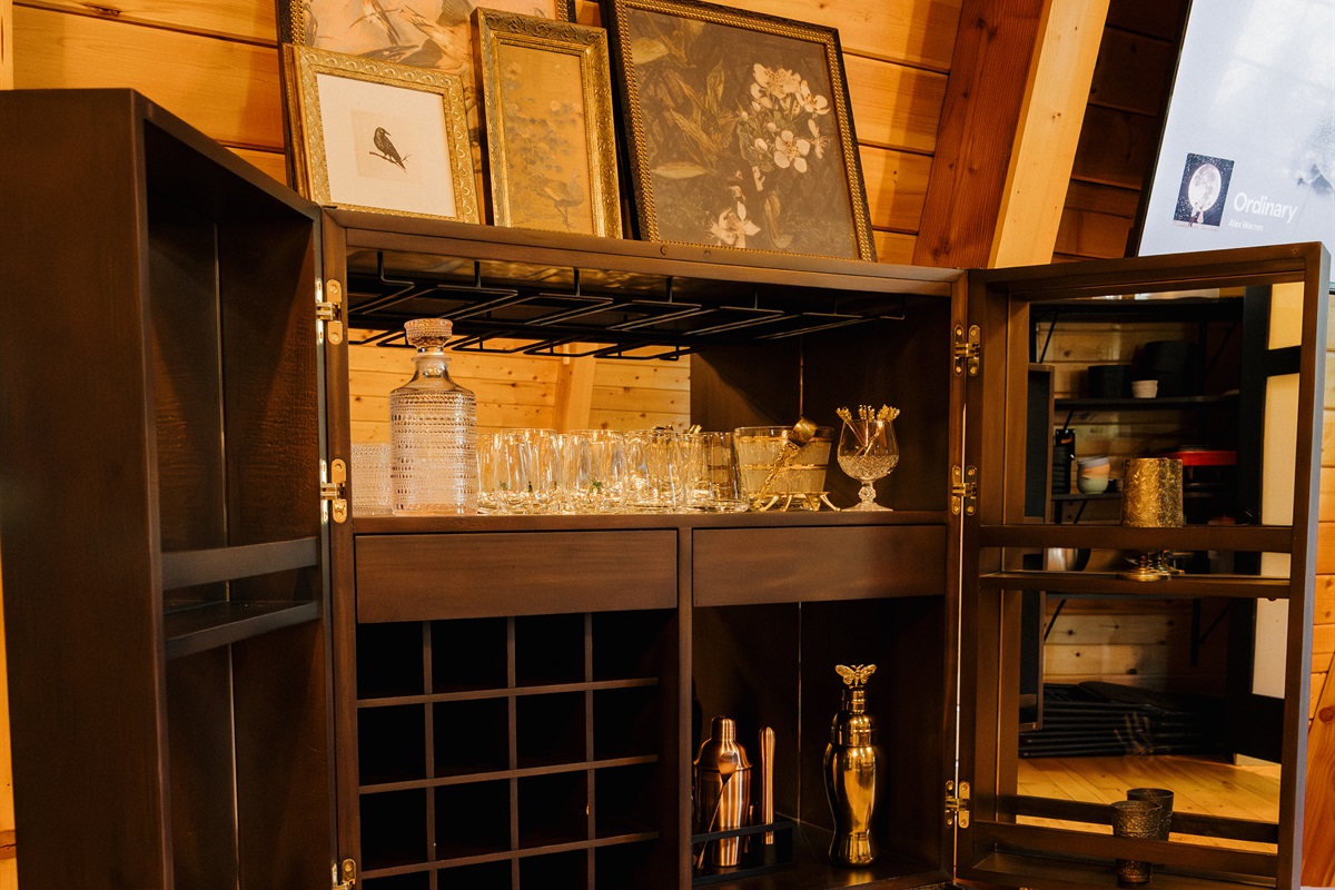 A curated bar cabinet stocked with glassware and barware awaits at Poppywood Pines. This gothic western Show Low A-frame blends luxury amenities with rustic charm, perfect for entertaining after days exploring White Mountains hiking trails and lakes.