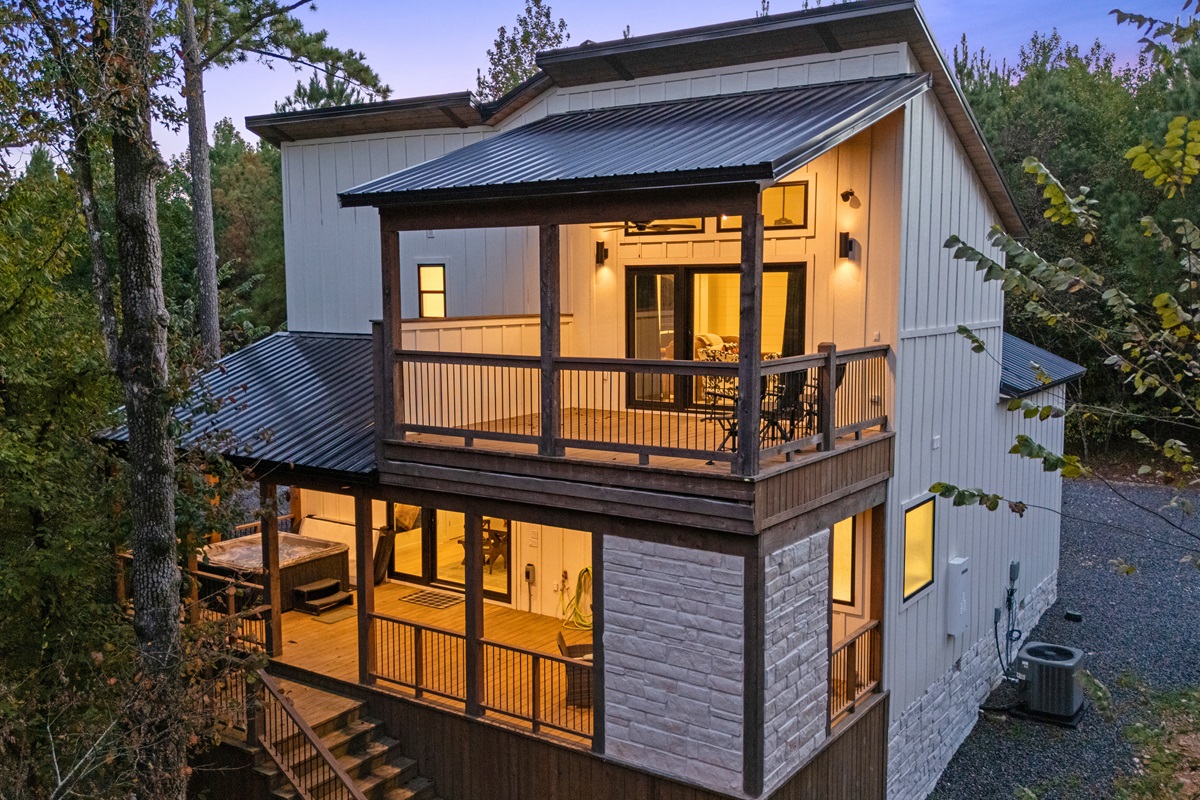 The back of the cabin glows warmly at dusk, with large windows and an upper deck overlooking the trees.