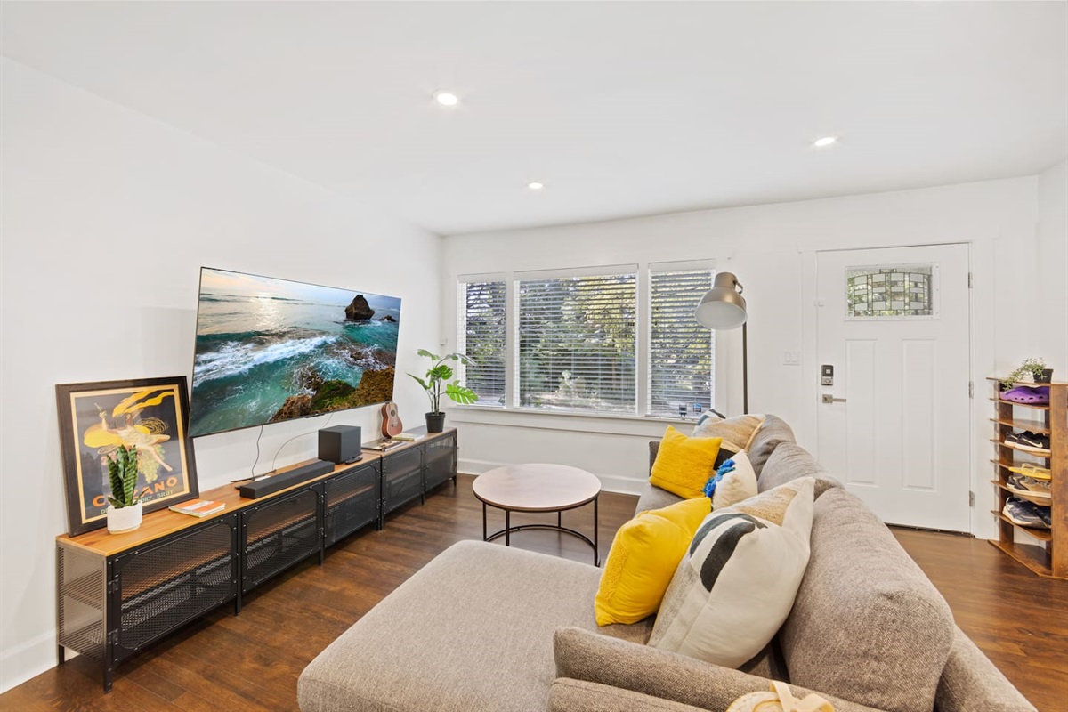 Living room with 70" smart TV and chaise lounge couch.  Large south facing windows let in a lot of natural light.