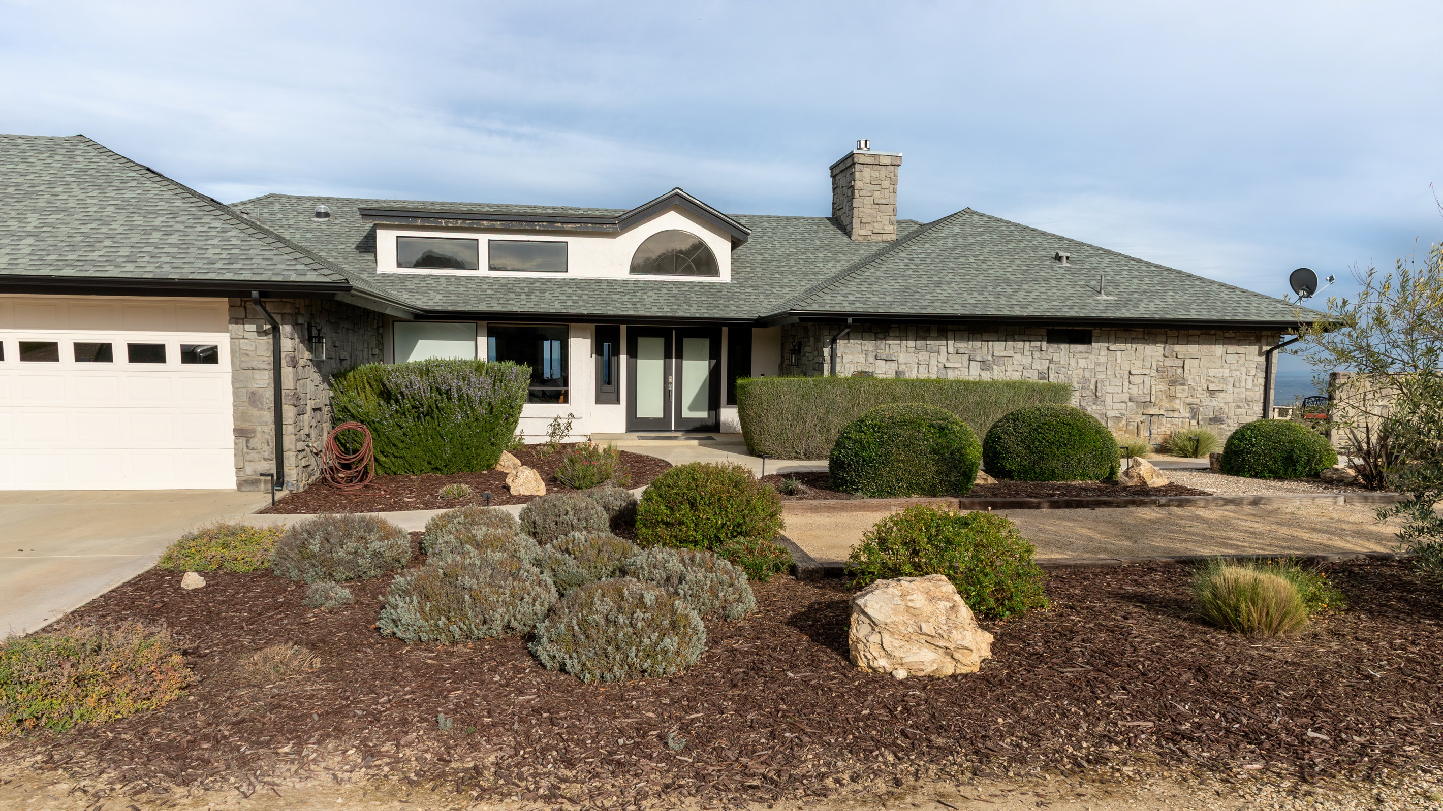 Welcome to the hilltop. The stone-clad exterior, manicured grounds, and classic arched window hint at everything waiting inside — and the valley views peeking out on the right tell the rest of the story.