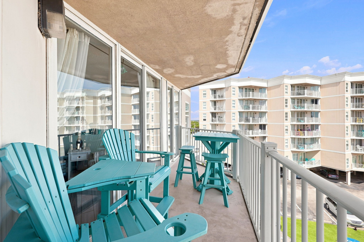 Private balcony furnished with teal Adirondack chairs, overlooking the resort grounds and surrounding coastline.