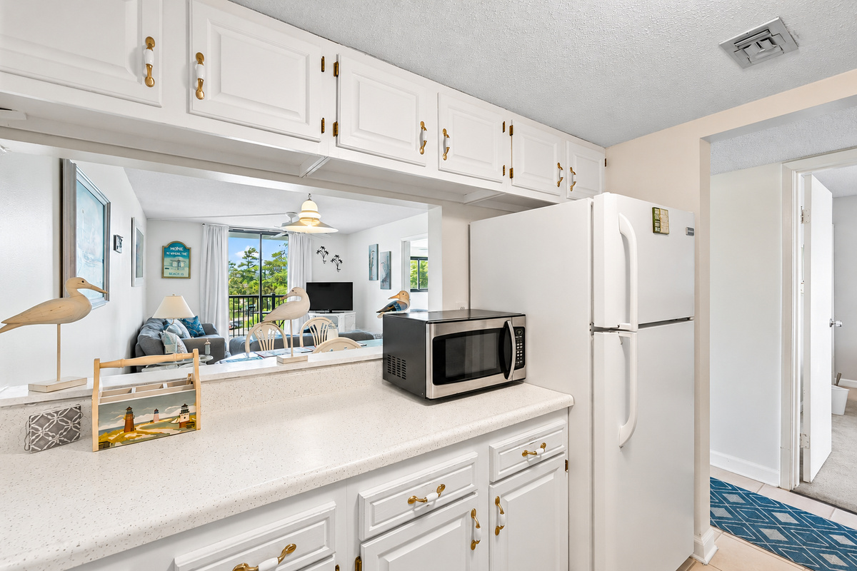 Kitchen with white cabinets, full-size fridge, microwave, and a pass-through view into the living room and balcony.