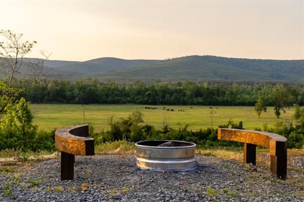 Fire pit area overlooking open pasture and mountain ridgelines.