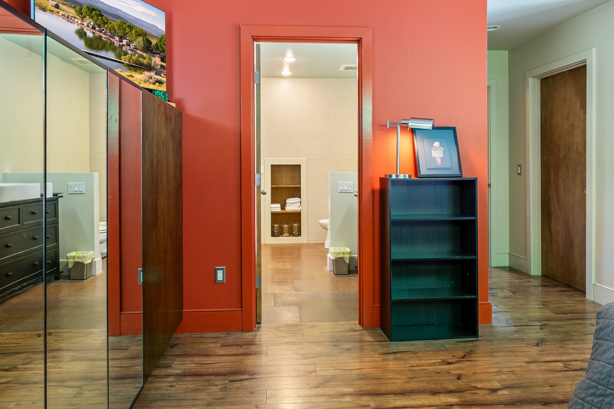 Private en-suite comfort at "The Crag." The main floor bedroom offers direct access to its spacious full bath, featuring bright tiled walls, built-in towel alcoves, a dark wood vanity, and a smooth, zero-threshold transition.