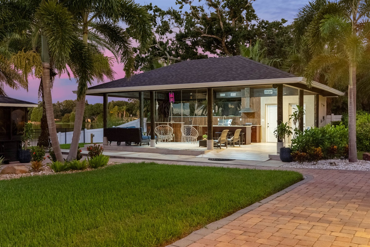 Relax under the warm glow of sunset in this covered outdoor living space, complete with cozy seating, a full kitchen, and panoramic waterfront views.