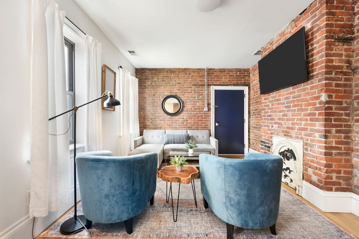 Enjoy a sophisticated atmosphere with a trendy brick wall, huge windows, and a thoughtfully designed space featuring a cozy sofa, coffee table, and accent chairs.