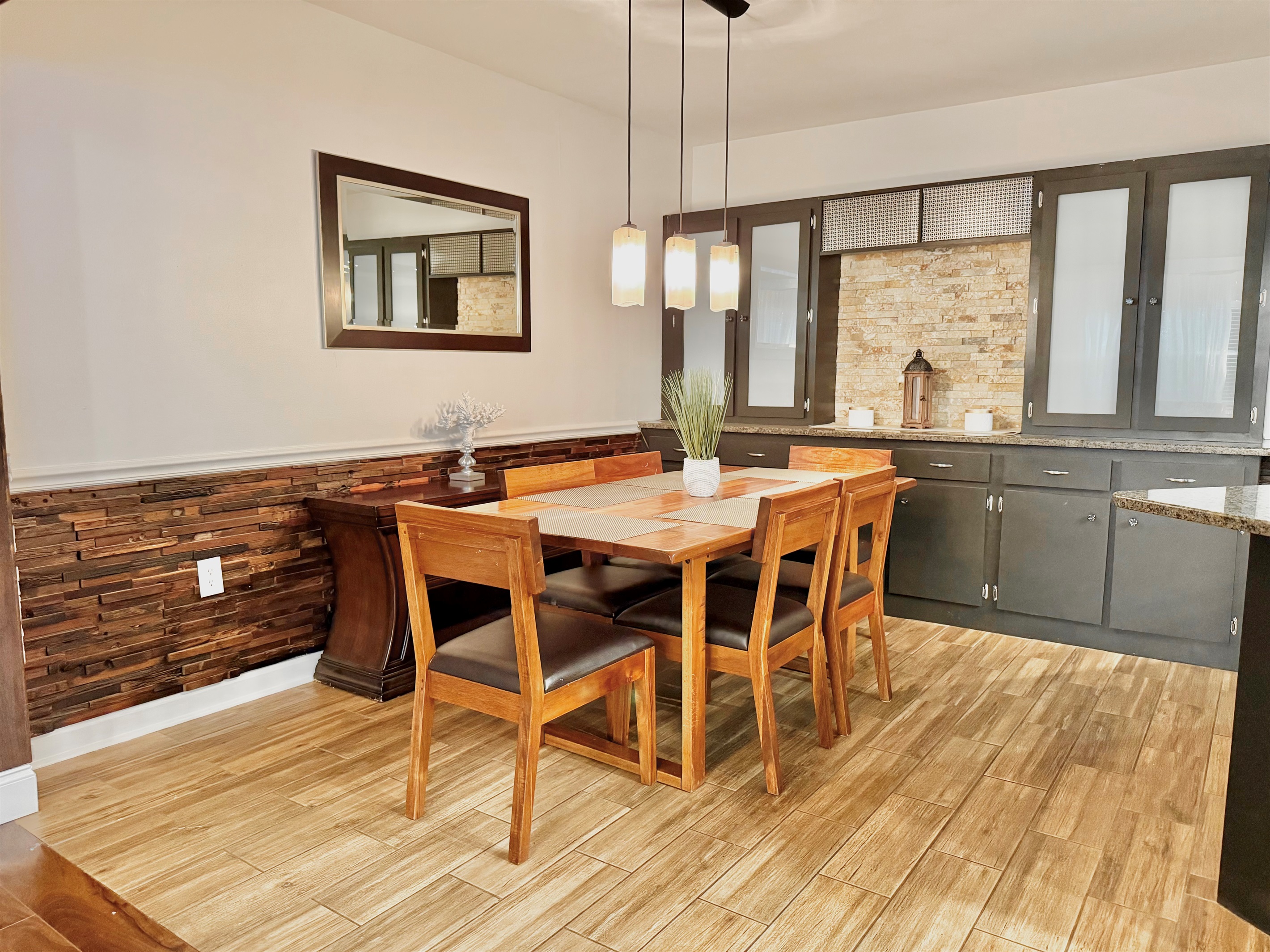 Enjoy cozy meals or family game nights around this modern wooden dining table, set under warm pendant lighting and open to both the kitchen and living room.