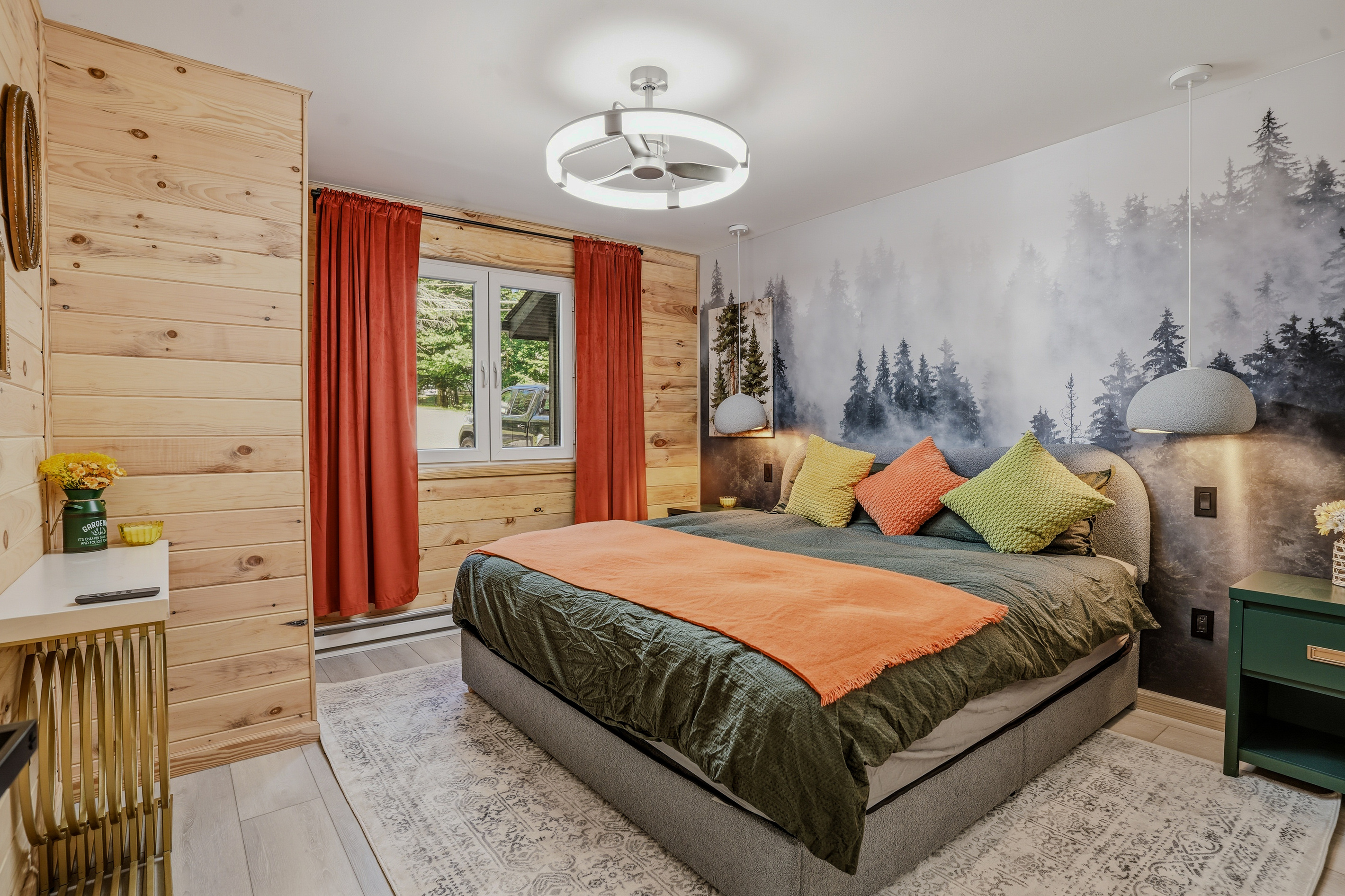 Bedroom with misty forest mural, orange bedding, and warm pendant lighting
