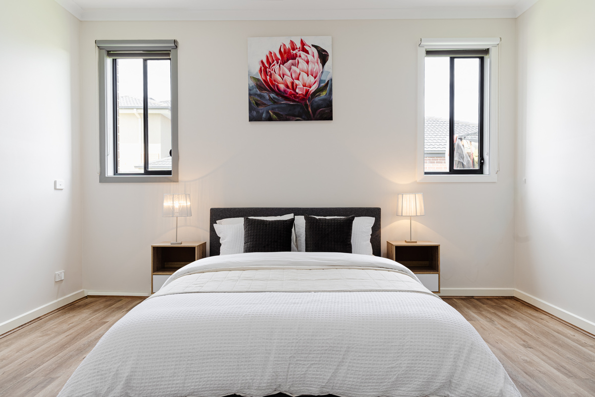 The bedroom includes a queen bed, bedside tables, lamps and two windows, creating a comfortable room within the home’s sleeping layout.
