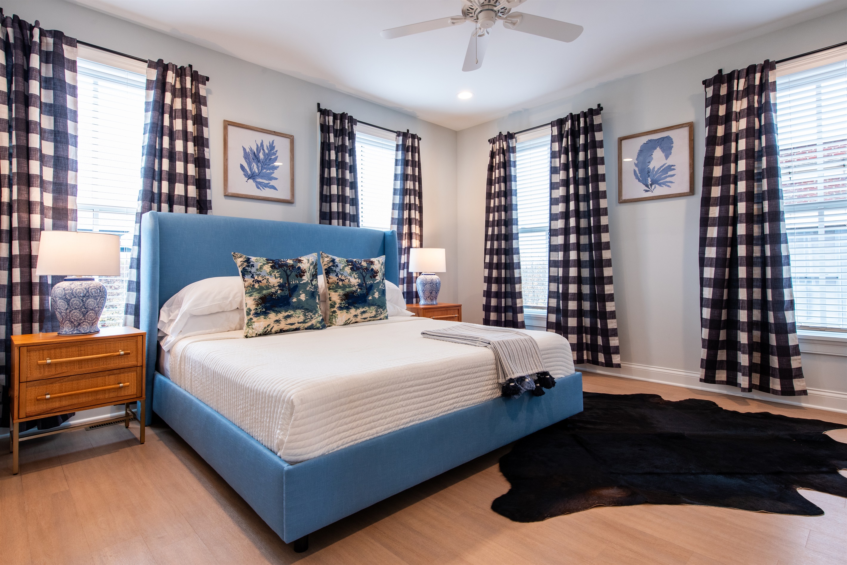 Relax in style in this beautifully appointed bedroom with a plush blue bed, elegant decor, and cozy furnishings. The room is bathed in natural light, framed by classic checkered curtains, making it the perfect spot for your stay on the Bourbon Trail.