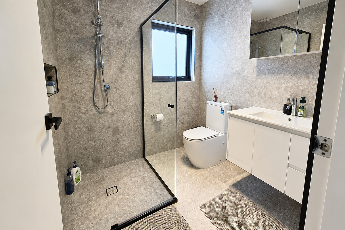 Matilda’s Urban Escape includes a full bathroom with grey floor-to-ceiling tiles, glass shower screen, vanity, mirror cabinet and toilet.