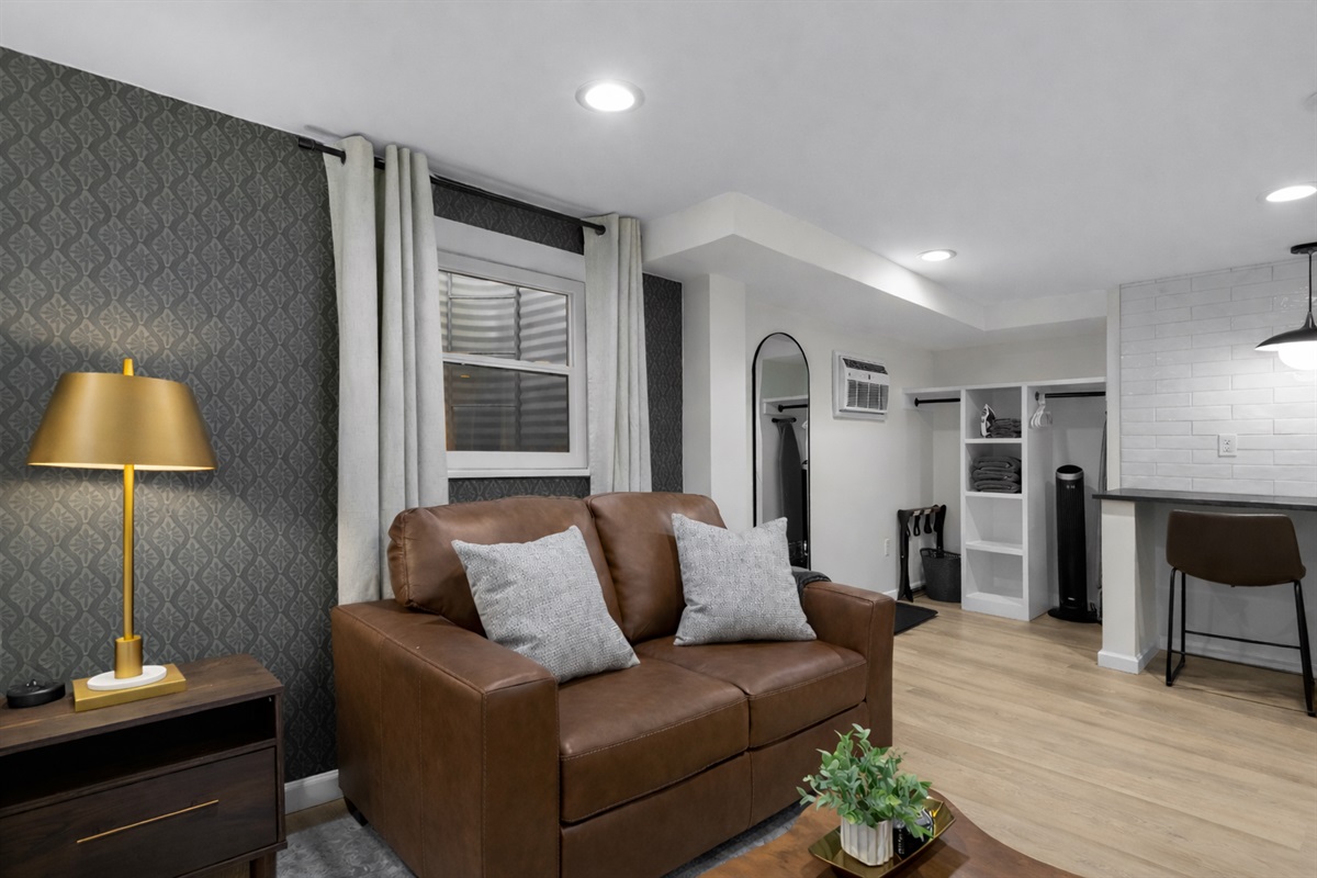 Spacious studio living area with cozy leather seating, warm lighting, and an open flow into the kitchen—perfect for relaxing, dining, and enjoying your stay.