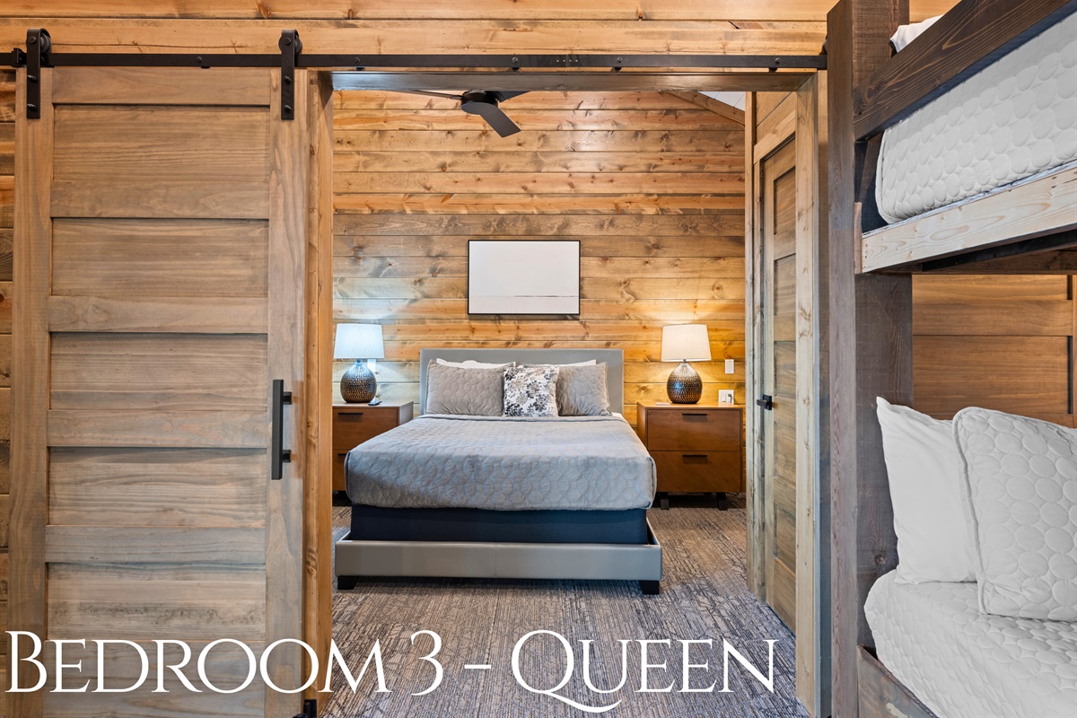 Bedroom 3: Queen bed with warm wood walls and barn door.