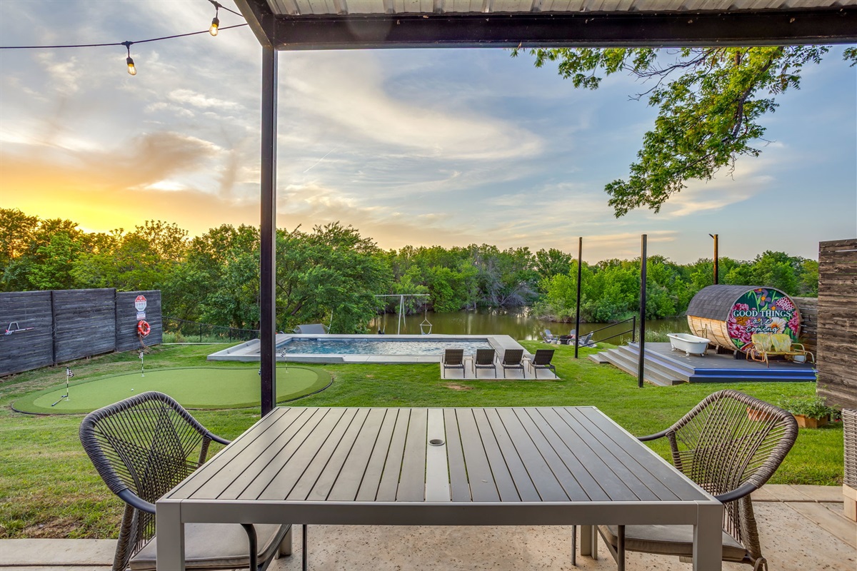 Covered outdoor dining overlooking a private pool, putting green, and lakefront views at The Noir, a luxury vacation rental on Lake Granbury, Texas.