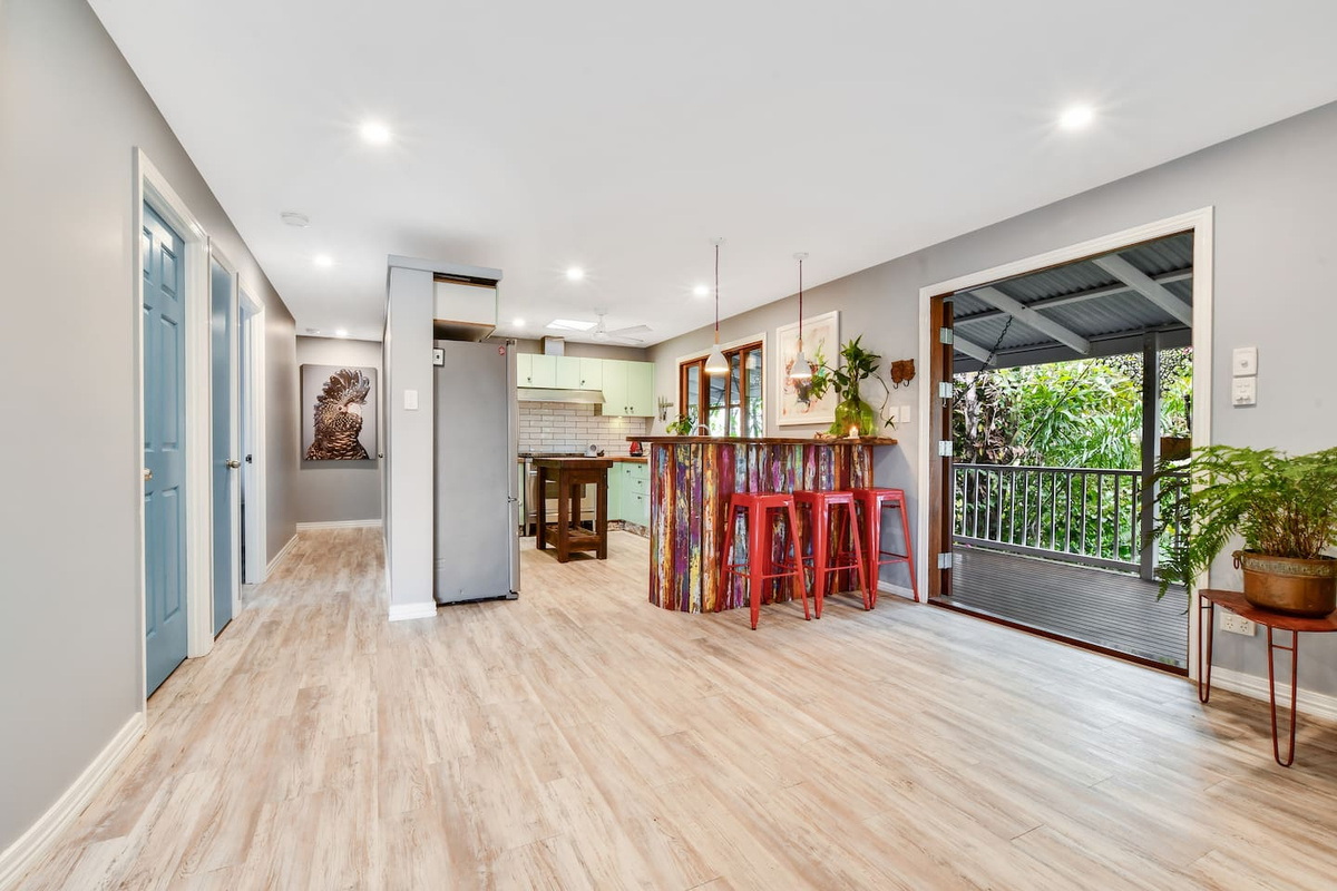 A vibrant timber bar, red stools and leafy outdoor outlook give this kitchen zone at Aaron's Beachside Boat House a distinctive, character-filled beach-house feel.