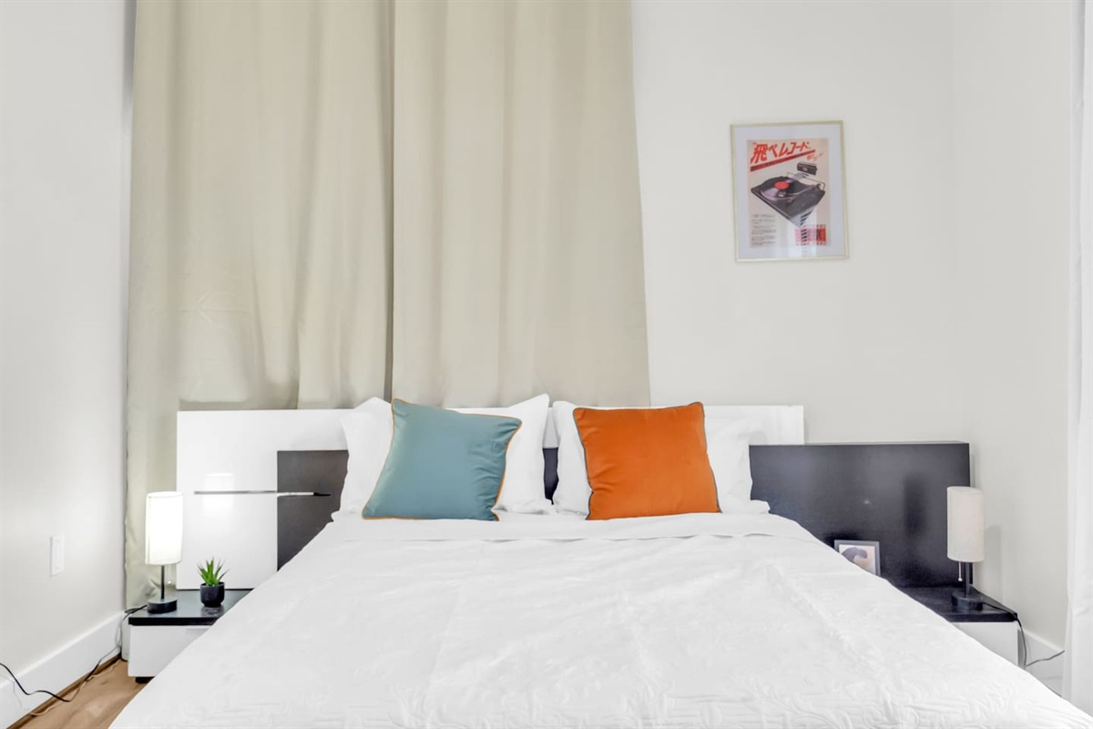 Bedroom with queen bed, warm lighting, room darkening shades and large window views.