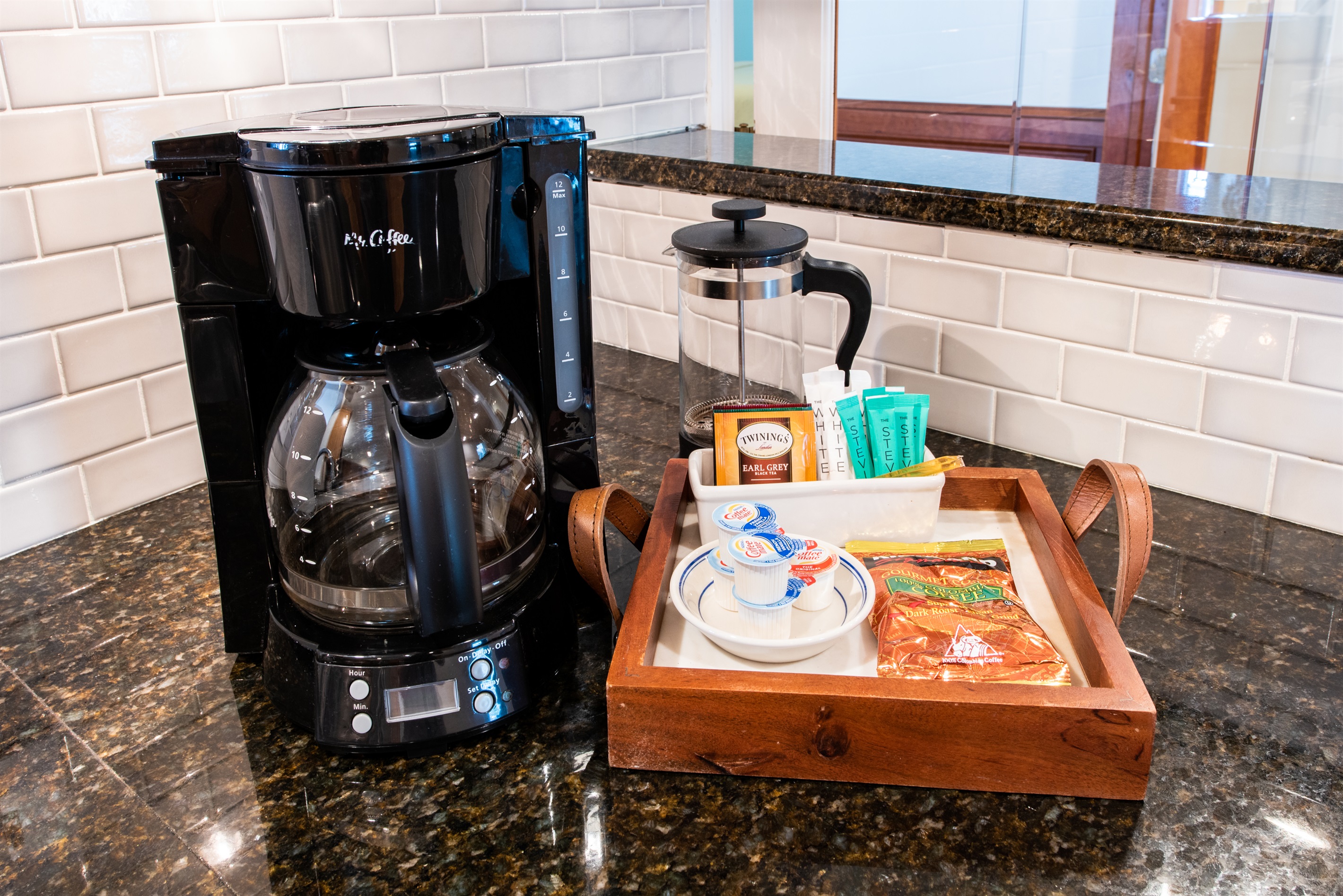 Start your Bourbon Trail day with our coffee station! Features a coffee maker, French press, & a tray with teas, creamers, & snacks on a sleek granite counter with white subway tile backsplash