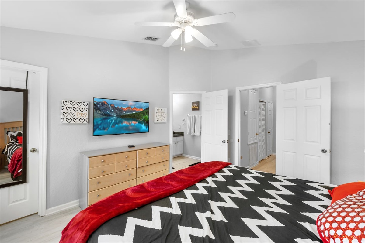 - Spacious bedroom with king bed, bold black and white chevron bedding, and red accents  
- Wall mounted TV and dresser for entertainment and storage convenience  
- Ensuite access and ceiling fan for added comfort and relaxation during your stay