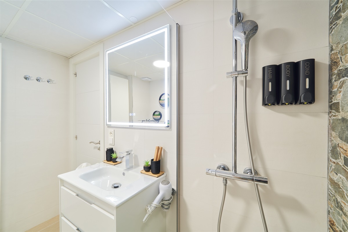 Modern bathroom with walk-in rain shower, stone accent wall, LED mirror, and fresh spa-like touches for your comfort.
