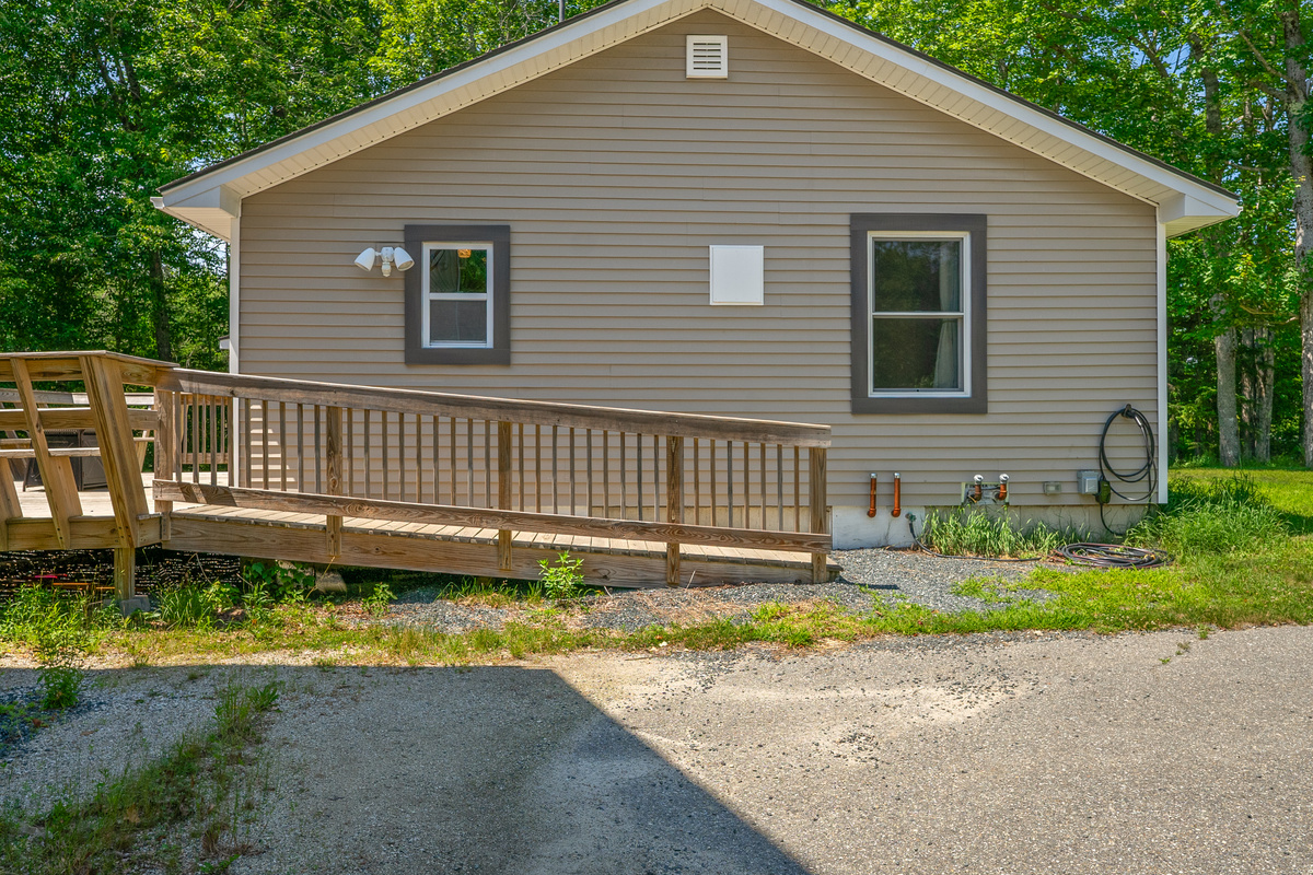 Detail view shows the Level 2 EV charging station beside the high-flow outdoor gear wash hose station. The long wooden entry ramp connects the driveway area directly up to the outdoor deck for convenient, stair-free access into the home.