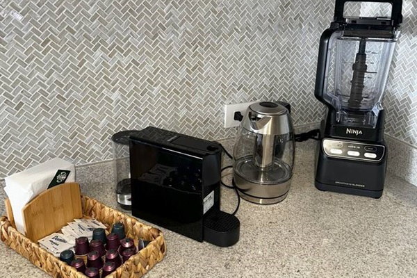 Elevate your mornings in this modern Cabo kitchen with a Nespresso Mini espresso machine, Sur La Table digital kettle with infuser, Ninja blender/smoothie maker, plus coffee pods, sugar, coffee, creamer, and tea—everything you need for your perfect drink.