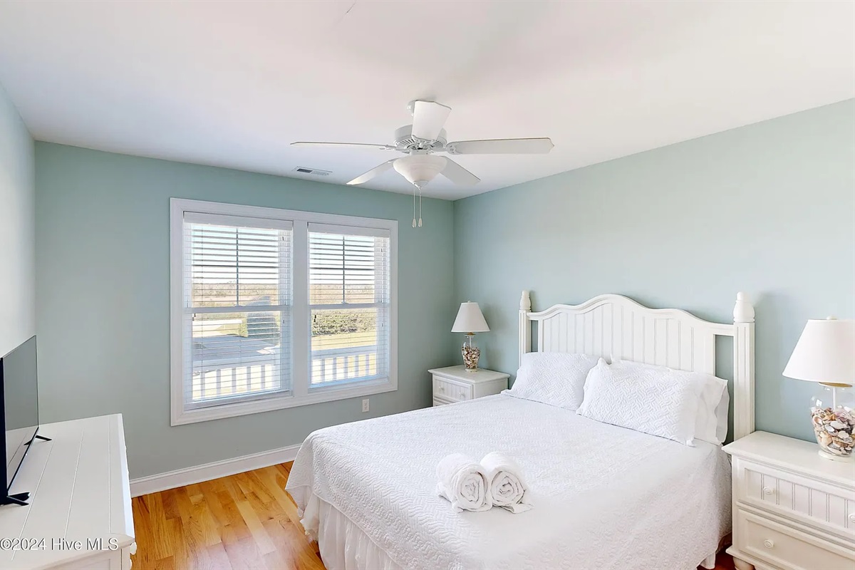 Bright and airy bedroom featuring a plush queen bed and ceiling fan
