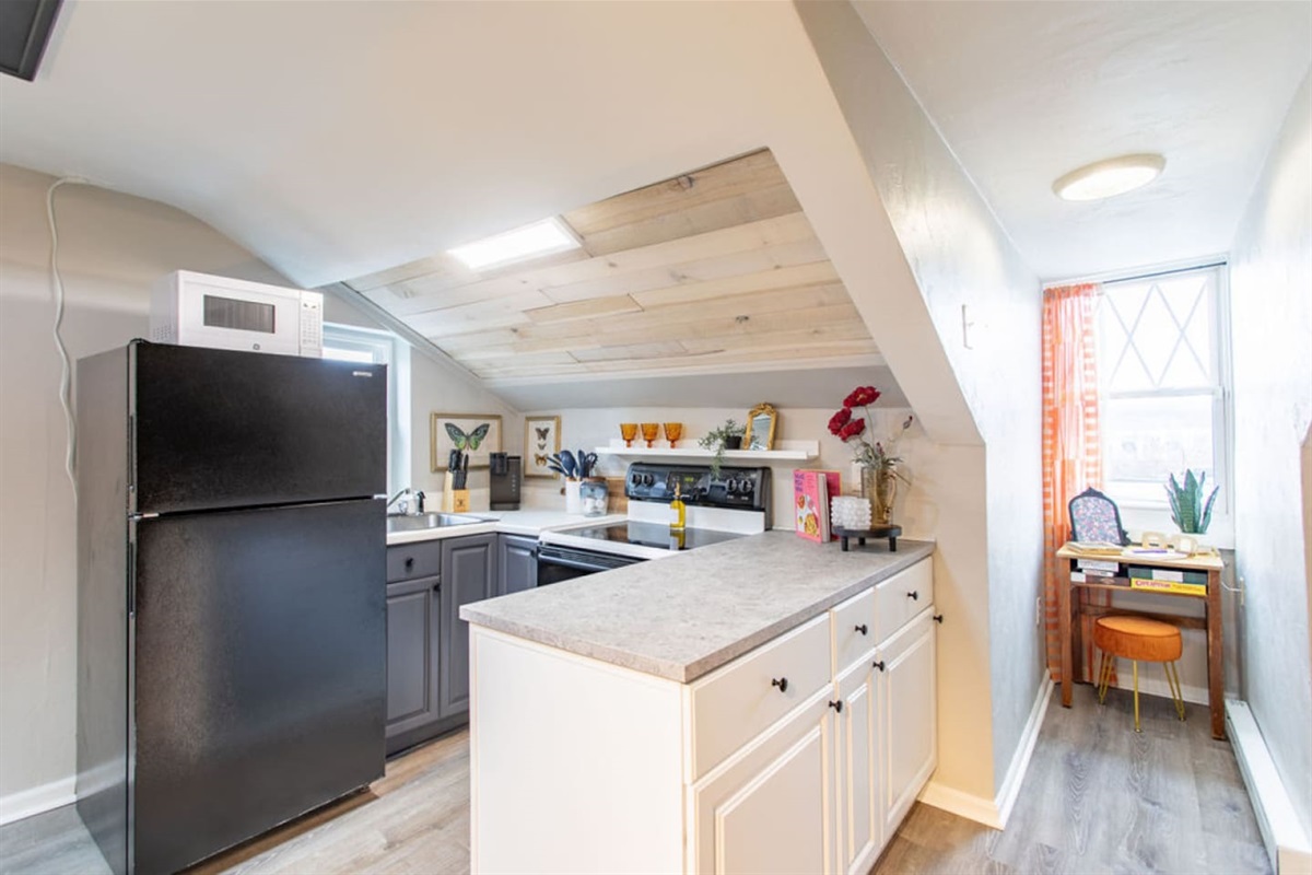 Prepare your meals in this cozy kitchen, equipped with essential appliances and a handy island for extra prep space. The charming window dormer on the right features a versatile desk, perfect for working, doing makeup, or simply enjoying the peaceful