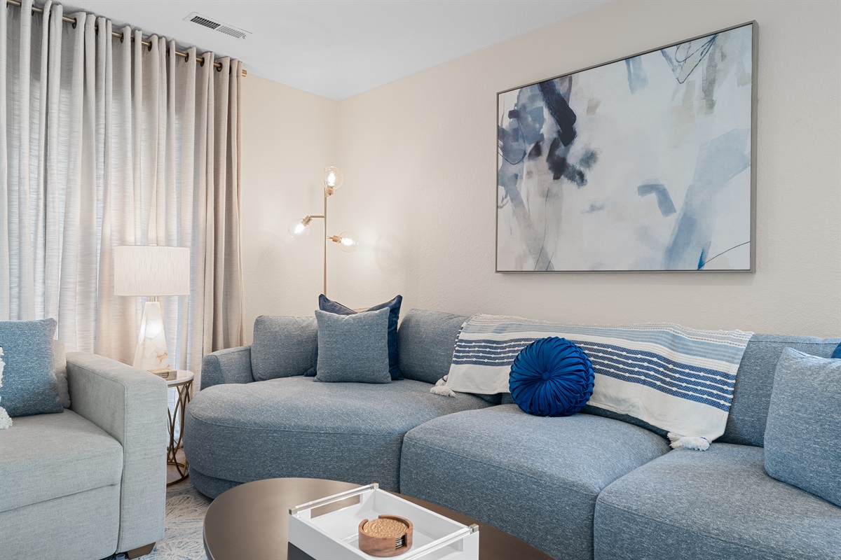 🎨 A modern aesthetic meets comfort in this chic living space, with abstract art, coordinated pillows, and a soft palette of greys and blues.