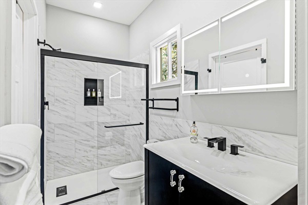 Guest bathroom with marble tile shower and flooring. LED lighted mirror above sink.