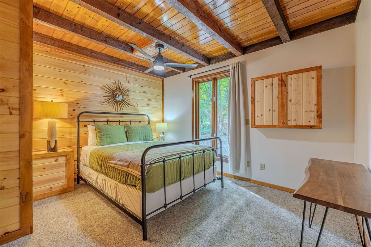 A well-appointed main-level queen suite with a ceiling fan, desk, and direct entry to the downstairs full bathroom for added convenience.