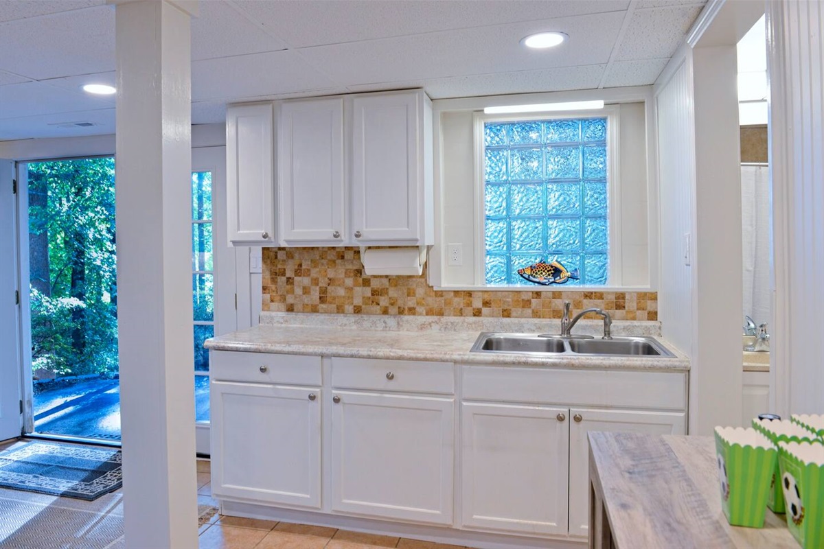 Basement level kitchen equipped with a microwave, sink and full size refrigerator.