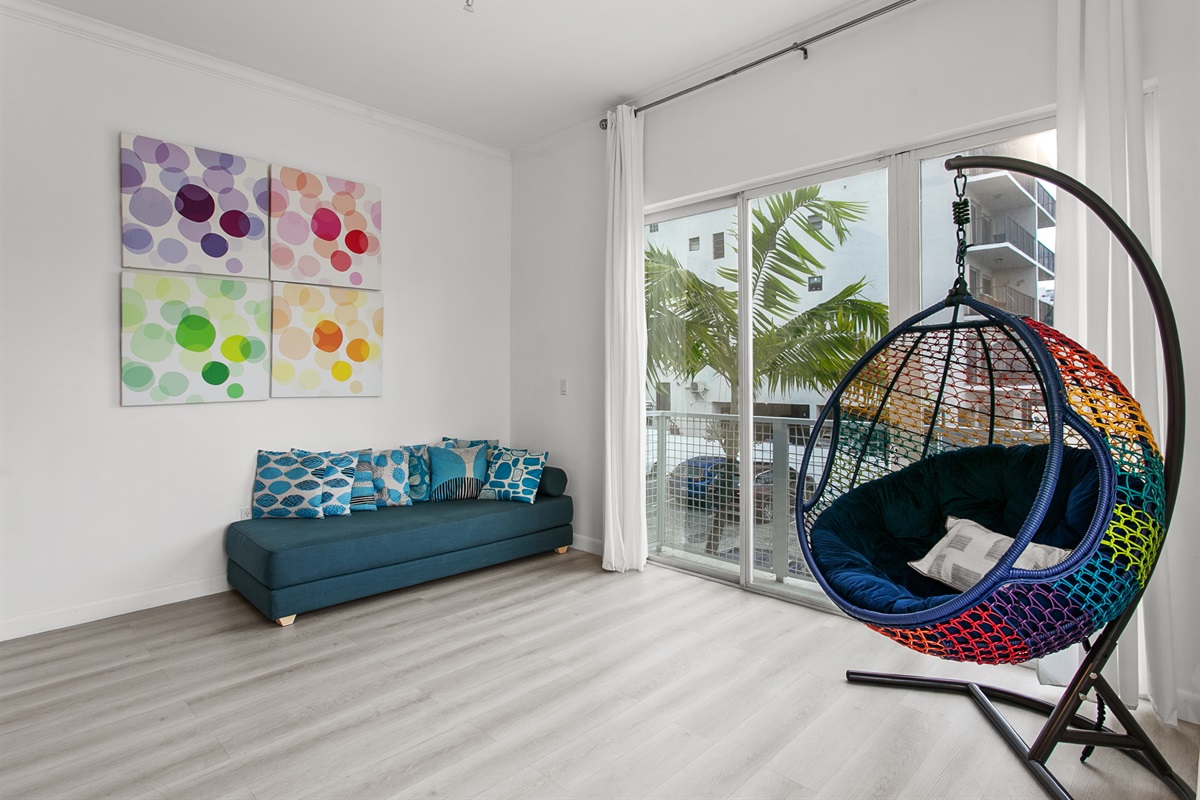 Huge sunny corner living room with two sofas, a daybed, and a swing chair. Private balcony with city and waterway views.