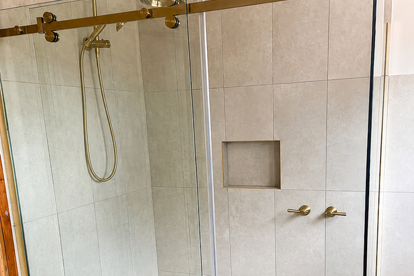 A glass walk-in shower, brass fittings, tiled walls and built-in niche give this bathroom a clean, easy setup for everyday use.