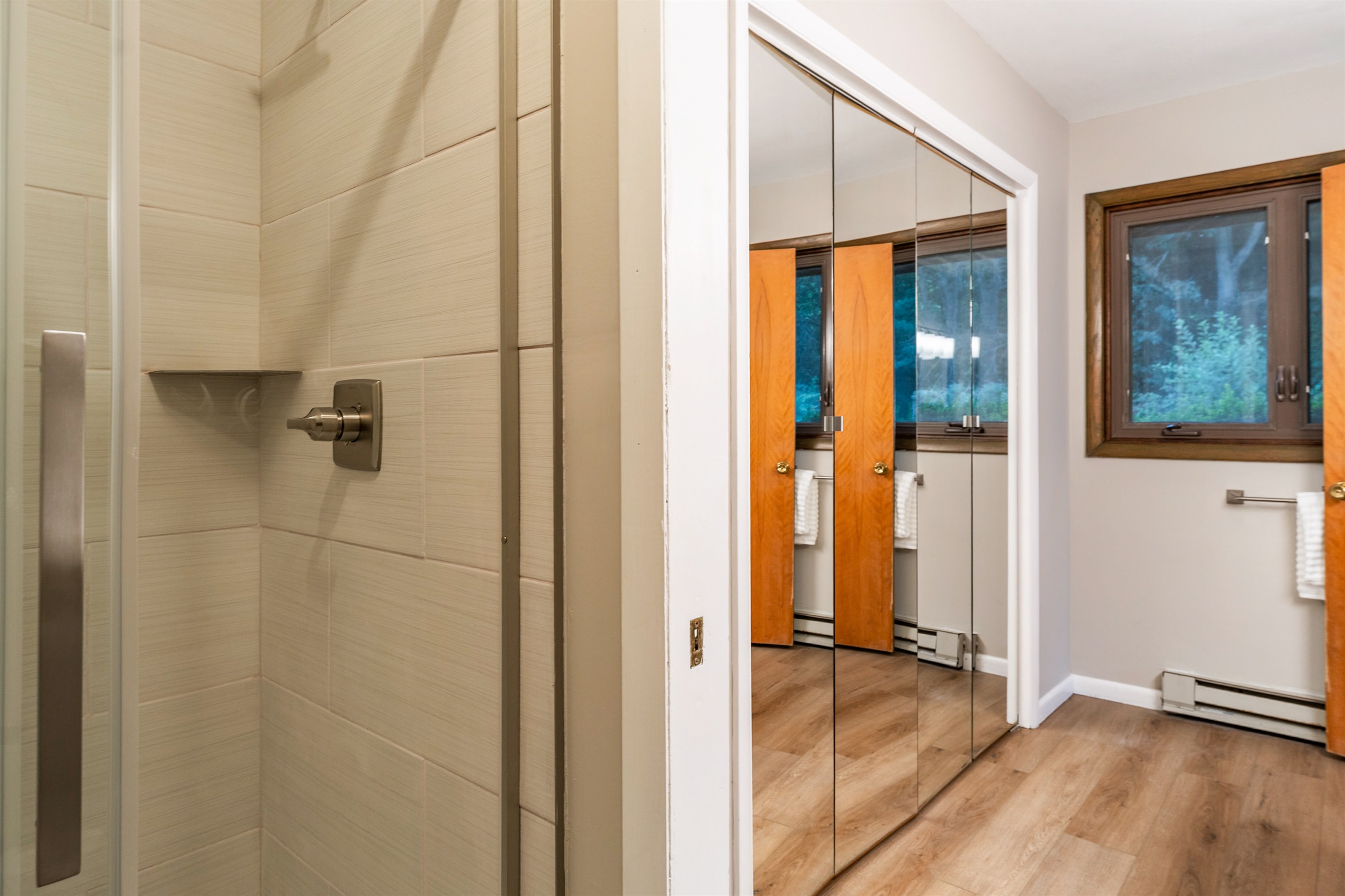 Freshly updated bathroom with modern tile shower and mirrored closet doors, creating a bright and spacious feel.