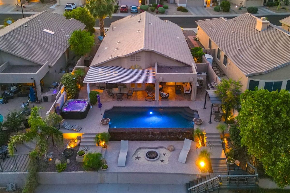 An aerial view reveals just how much this backyard has to offer — a private pool, hot tub, covered patio, fire pit, and direct lake access, all in one stunning outdoor retreat.