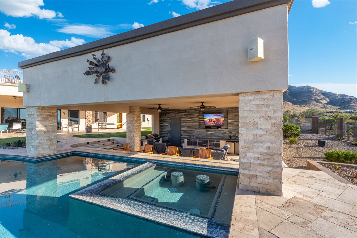 Covered outdoor lounge beside the pool with shaded seating and TV — relax in comfort between swims and sunsets