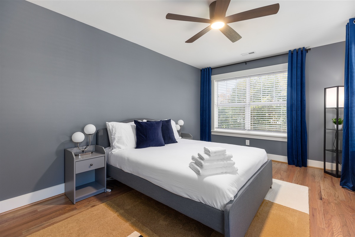 Spacious queen bedroom upstairs has plenty of pillows, blackout curtains, and an overhead fan for a good night's sleep.