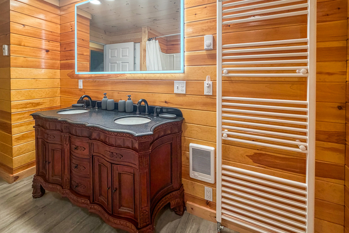 Wrap yourself in comfort using the large wall-mounted heated towel warmer rack. This perspective highlights the spacious double vanity setup complete with an illuminated LED mirror, elegant wood-carved base, and a convenient wall-mounted heater.