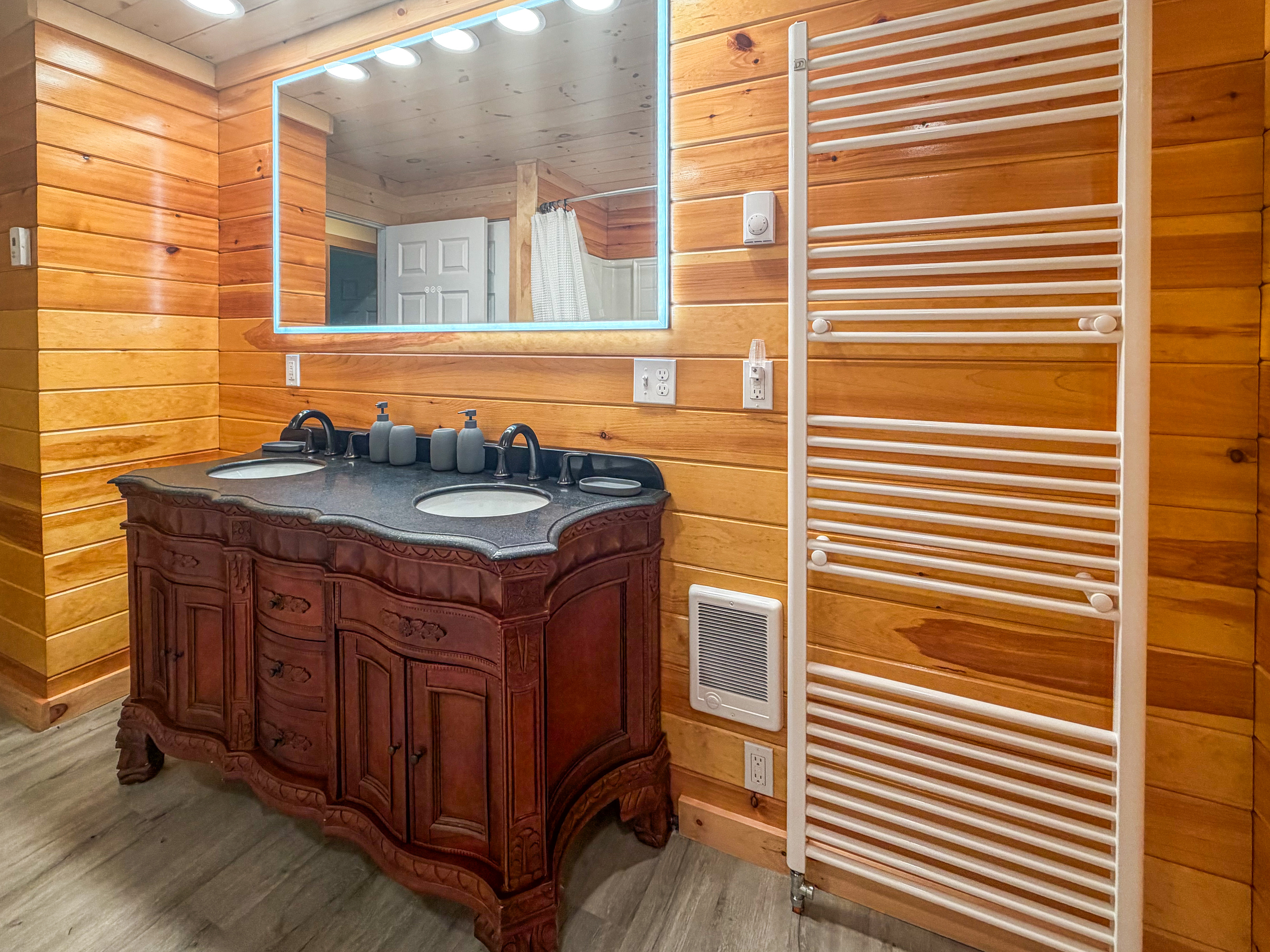 Wrap yourself in comfort using the large wall-mounted heated towel warmer rack. This perspective highlights the spacious double vanity setup complete with an illuminated LED mirror, elegant wood-carved base, and a convenient wall-mounted heater.