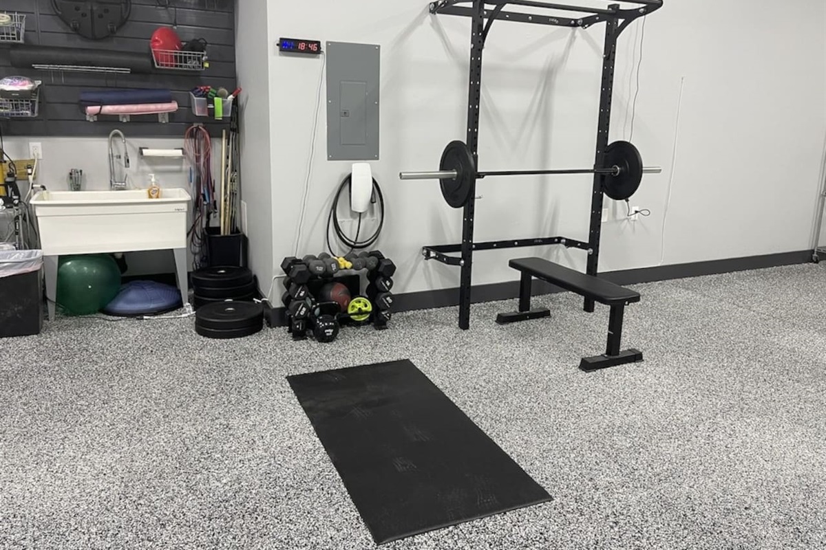 Squat rack, dumbbells, weight bench, kettlebells, and tesla charger in garage