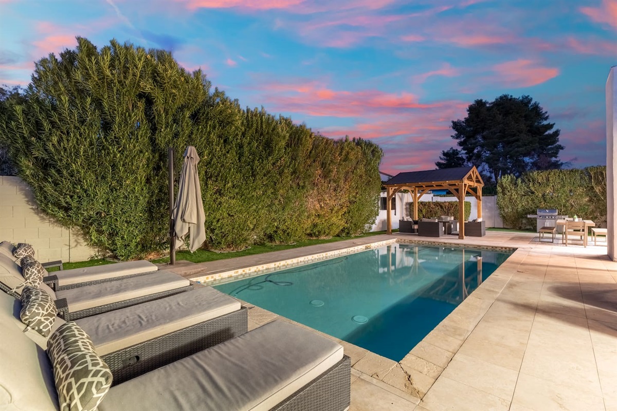 Lounge beneath cotton-candy skies on modern chaises, with views of the cozy fire-lit pergola and lush greenery all around.