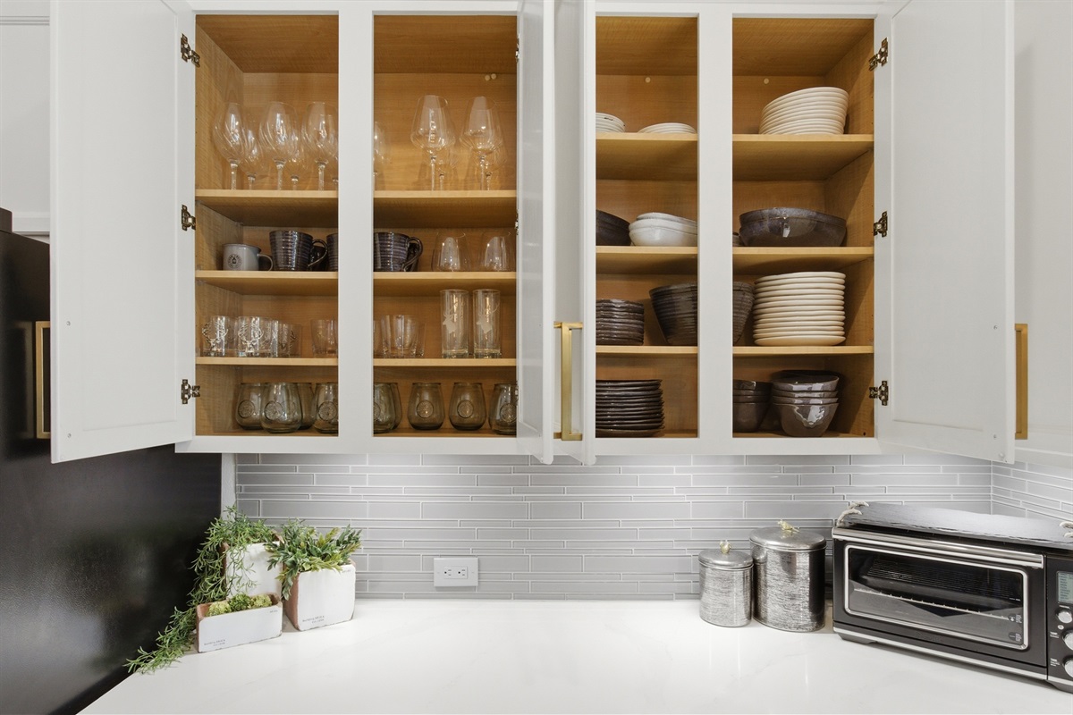 Open cabinets revealing fully stocked Wine Glasses, dishes, mugs, and serveware. Ready for entertaining or family dinners in.
