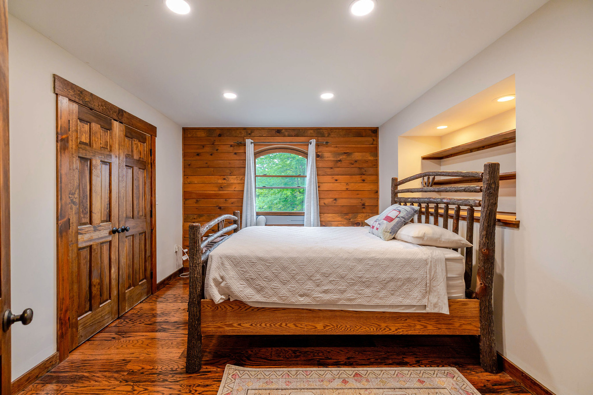 This cozy bedroom features a charming rustic ADK bed, warm wood accents, and a peaceful setting overlooking the heart of the home.