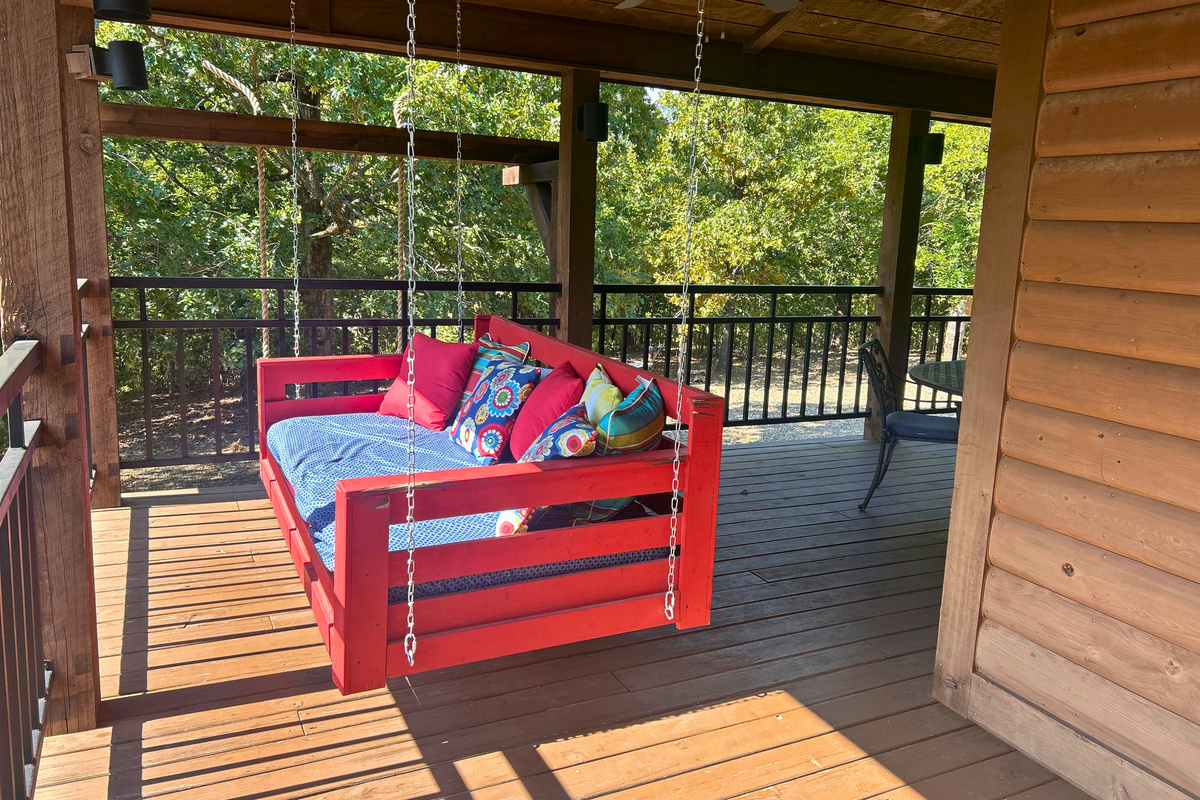 Step onto the deck and settle into the bright red porch swing, a cozy little spot for enjoying the fresh air and quiet forest setting.