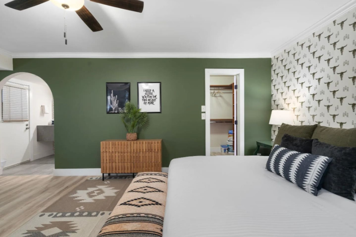 Tucked behind the bed, a walk-in closet and private bath keep this room feeling like its own suite. The olive green wall and framed prints add just enough personality without overwhelming the space.
