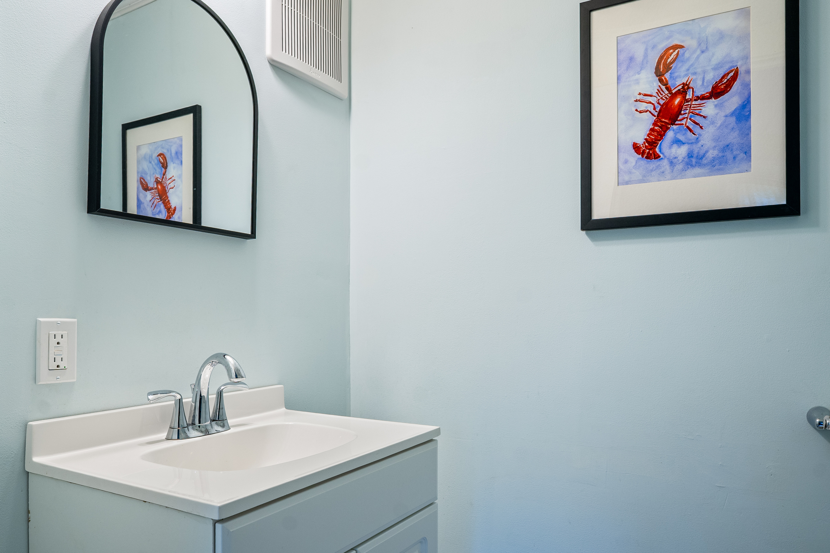 This closer perspective highlights the clean powder room vanity and modern arched mirror. Complete with a chrome faucet and a handy wall outlet right at the sink, this first-floor setup makes it easy for your group to refresh between activities.