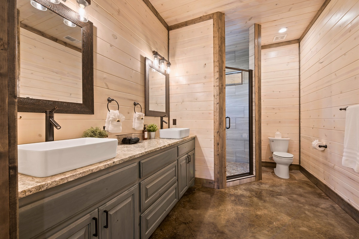 The bathroom extends into a walk-in shower, with glass doors emphasizing the space's clean lines and modern design.