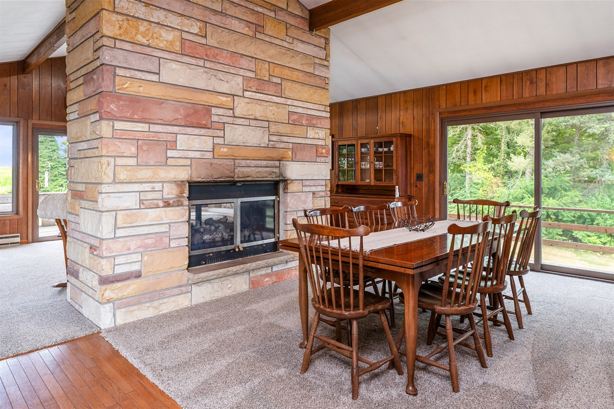 Enjoy cozy dinners by the stunning stone fireplace in this open-concept dining space, blending rustic charm with modern comfort.