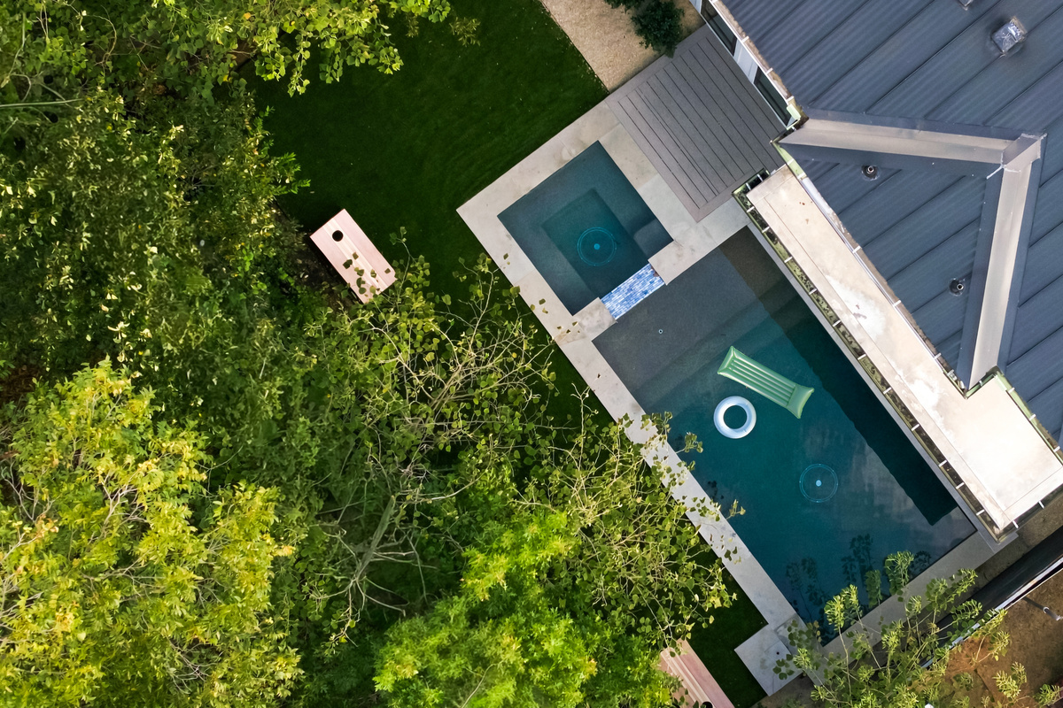 Aerial view captures the pool, turf yard, and cornhole setup from above.