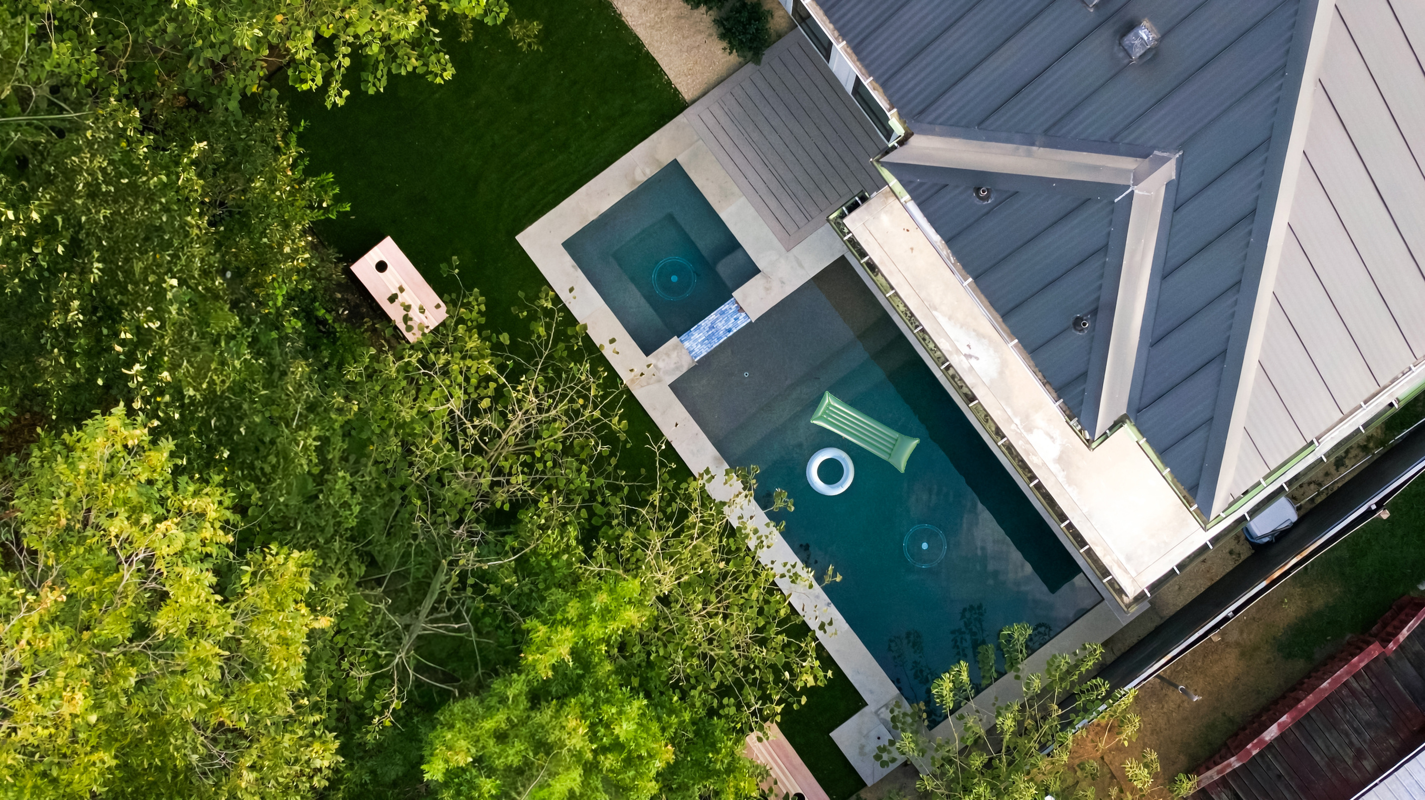 Aerial view captures the pool, turf yard, and cornhole setup from above.